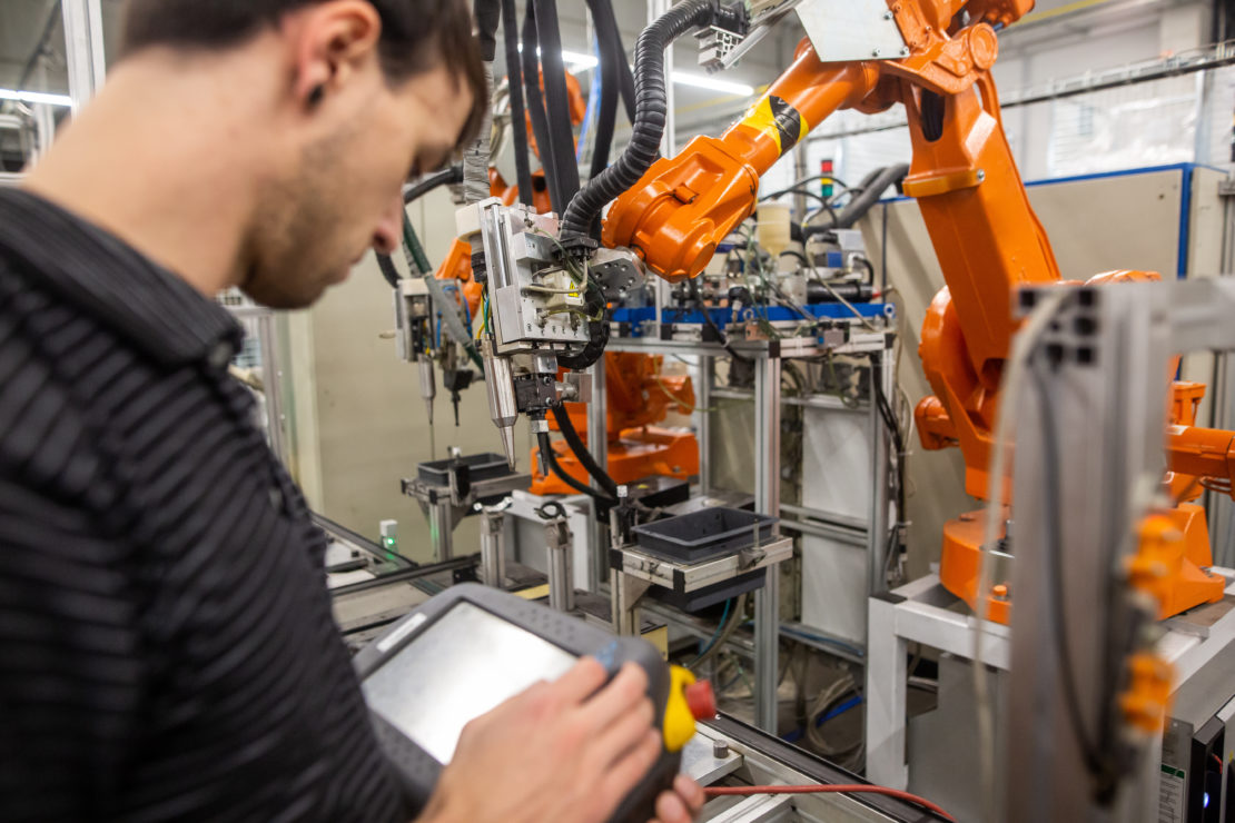 an automotive technician programs an orange industrial robot