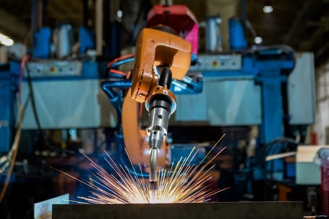 Picture of a yellow industrial robot welding a car body in an automotive manufacturing plant